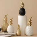 Golden resin ornament in the shape of a pineapple, displayed in a room setting, featuring natural elements like plants and twigs.