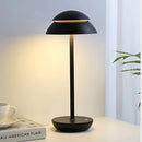 Scandinavian design table lamp in black, featuring a radiant light, placed on a table with white tableware including a coffee cup surrounded by plants.