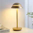 Scandinavian design table lamp in gold, featuring a white shade and a wooden base, complemented by a coffee cup and a plant on a table, enhancing a modern interior design.