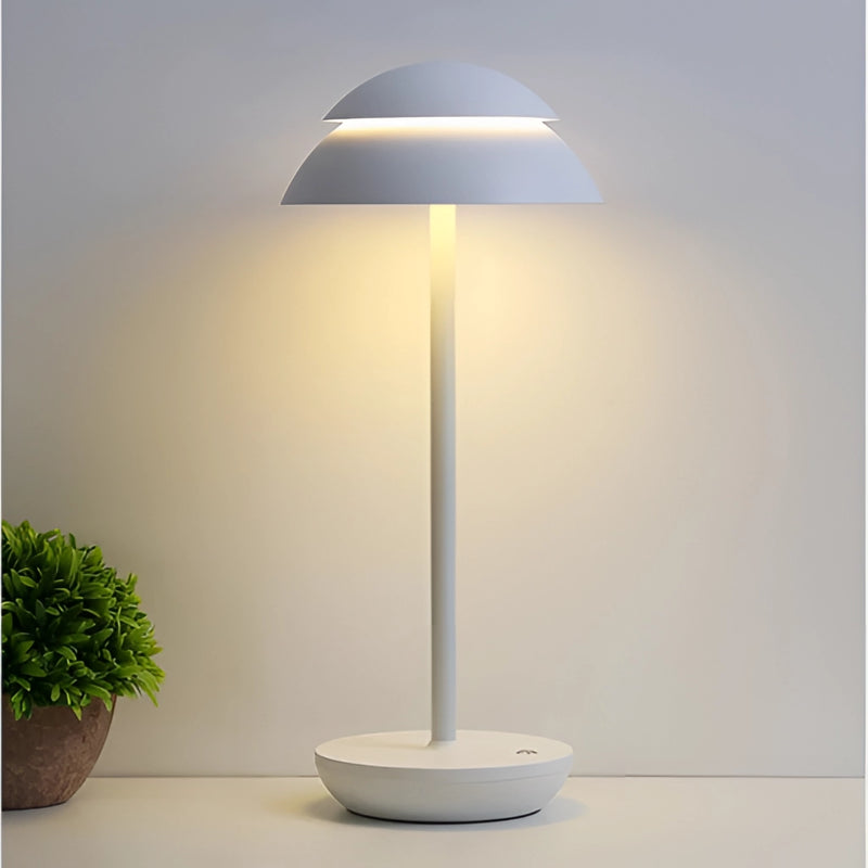Scandinavian design table lamp in white, placed on a wooden table next to a houseplant in a flowerpot, providing a soft light with artistic shades.