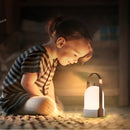 Toddler smiling and tapping a rechargeable table lamp with touch dimming feature on a wooden floor, creating a moody ambiance with shades and reflections.