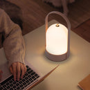 Rechargeable table lamp with touch dimming feature on a wooden surface, beside a laptop in an office setting.