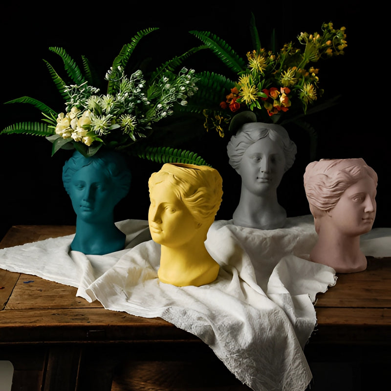 Blush pink resin vase designed in the neoclassical Venus style, featuring intricate floral arrangements and detailed sculptural elements like heads, eyes, and hairstyles.