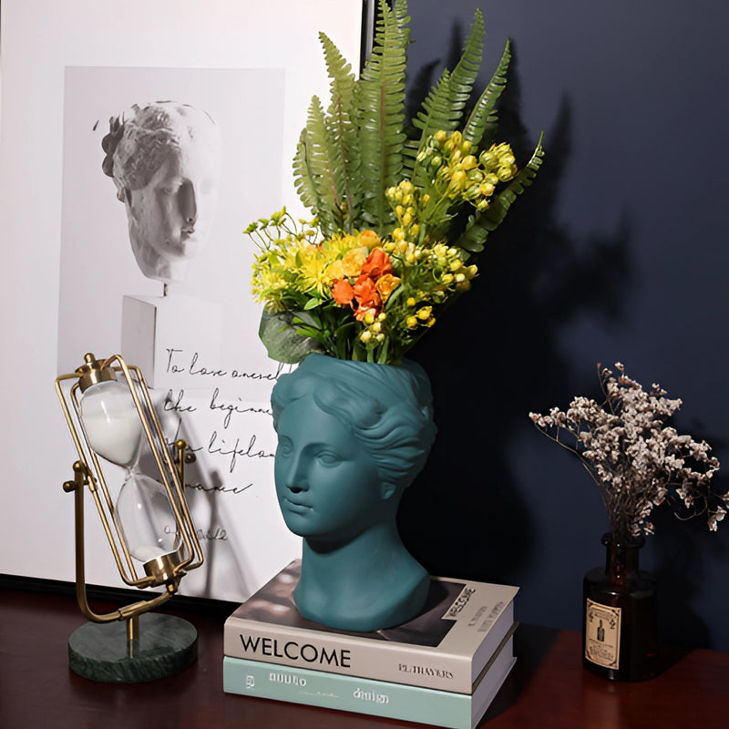 Resin Neoclassical Venus Vase in blush pink, teal, and grey with a houseplant and artistic floral arrangement.