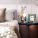 Resin table lamp featuring an elegant rabbit girl design with dual glass lampshades, decorated with textile patterns and wooden elements in a cozy room setting.