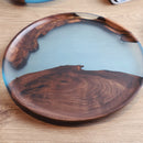 Handcrafted epoxy resin plate with natural wood design, displayed on a table, featuring a circular shape and resembling serveware or dishware.