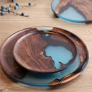 Handcrafted epoxy resin and wood tray featuring blue tones and natural patterns, used as creative tableware or serveware.