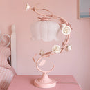 Elegant Rose Encased Table Lamp featuring a pink floral design in a metal frame, displayed on a wooden table.