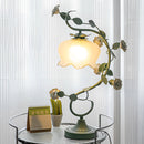 Green rose encased table lamp with twig and plant design elements, providing a soft yellow light, ideal for elegant interior lighting.