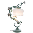 Elegant table lamp featuring a metal lampshade with a rose and twig design, placed on a table as a decorative and functional lighting accessory.