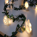 Battery-operated LED garland featuring rose flowers, elegantly draped over a table with intertwined twigs and soft lighting, enhancing an intimate interior design.