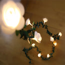 Battery-operated LED garland featuring rose flower string lights, elegantly draped over branches, displaying a variety of tints and shades under a dimly lit ceiling.