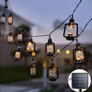 Warm white solar string lights with 50 LED lanterns draped over trees, illuminating a garden setting under a cloudy sky, IP65 waterproof.