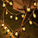 Outdoor solar string lights featuring LED lanterns in RGB and white colors, displayed on a wooden structure with ambient amber lighting, IP65 waterproof.