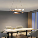 Elegant spiral pendant light providing warm illumination, displayed above a wooden table in a modern interior setting with wooden flooring.