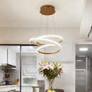 Elegant spiral pendant light providing warm illumination, displayed above a wooden table with a vase and flowerpot, enhancing the modern interior design of the room.