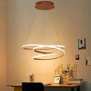 Elegant spiral pendant light with warm illumination, featuring an aluminum design, displayed over a wooden table in a well-designed interior setting.
