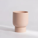 Large misty rose ceramic vase stacked with various bonsai on a wooden table.