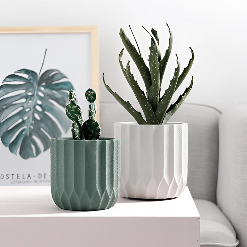 Textured ceramic polygon vase with a geometric design, displayed on a couch surrounded by various houseplants.