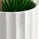 Textured ceramic polygon vase with a geometric design, featuring plants and a flowering plant in a flowerpot, set against linens with visible plant stems and lines.