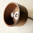 Walnut wood pendant lamp inspired by Japanese woodworking, featuring a circular plywood design with metal rim, hanging from the ceiling.