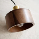 Walnut wood pendant lamp inspired by Japanese woodworking, featuring a circular wooden design with metal accents, hanging over a table.