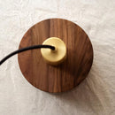 A walnut wood pendant lamp inspired by Japanese woodworking, featuring a circular design and a smooth, varnished finish, hanging over a table.