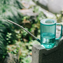 Blue metal watering can with an extended spout, positioned on grass.