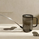 Stainless steel watering can with extended spout on a wooden table, designed for precise water delivery to plants.