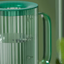 Green watering can with extended spout on a table, designed for accurate water delivery.