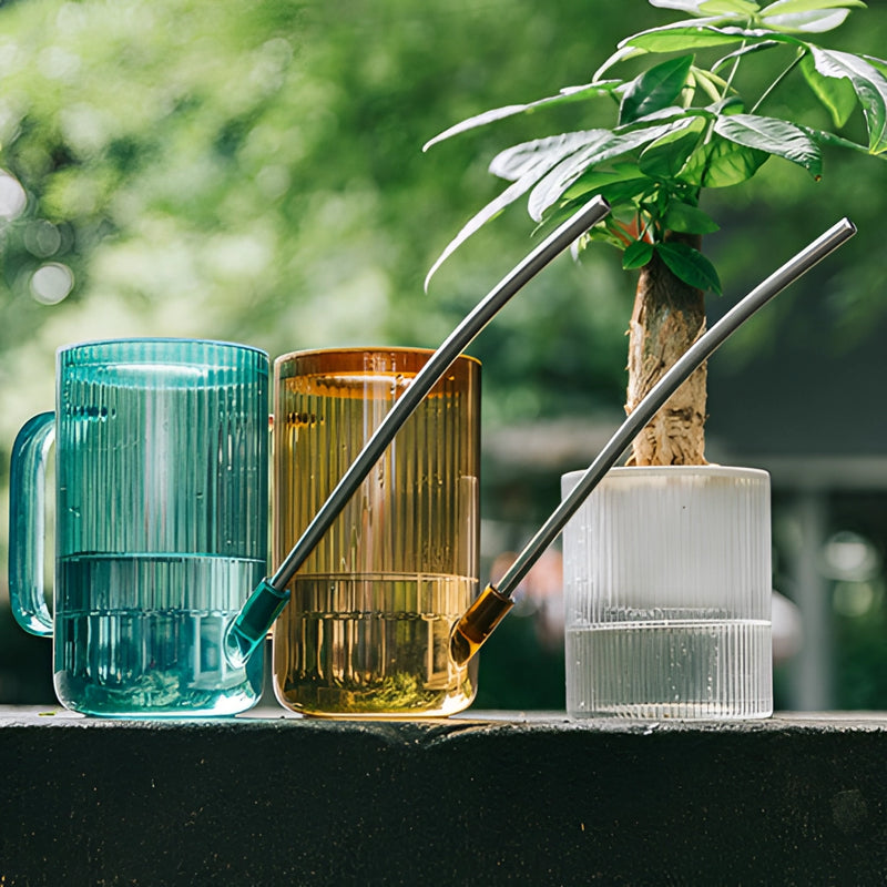 Watering can with extended spout on grass next to plants, designed for accurate water delivery.
