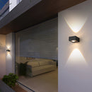 Black UFO-shaped waterproof wall light mounted on a grey wall near a wooden floor with a couch in the background.