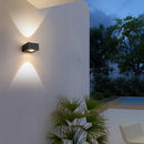 Black UFO-shaped waterproof wall light mounted on a wooden surface, surrounded by plants under a clear sky.