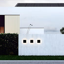 Outdoor wall-mounted waterproof LED light fixture made of aluminum, installed beside a window on a building facade, surrounded by plants and trees in an urban setting.