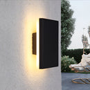 Outdoor wall-mounted LED lamp made of aluminum, illuminating a building facade with trees and plants nearby.