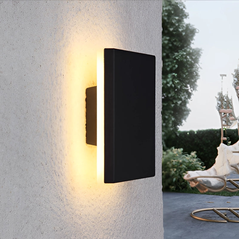 Outdoor wall-mounted LED lamp made of aluminum, illuminating a building facade with trees and plants nearby.