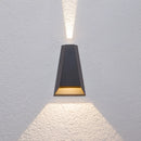Black waterproof outdoor pyramid LED wall sconce with warm white light mounted on a wooden surface, showcasing a symmetrical design and metal accents.