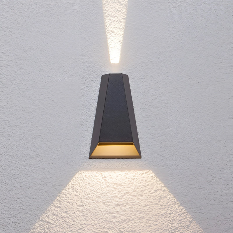 Black waterproof outdoor pyramid LED wall sconce with warm white light mounted on a wooden surface, showcasing a symmetrical design and metal accents.
