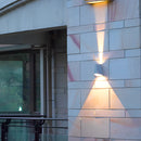 Pyramid-shaped LED wall sconce mounted on a wooden facade of a building, enhancing the architectural beauty with its shade and lighting effects.
