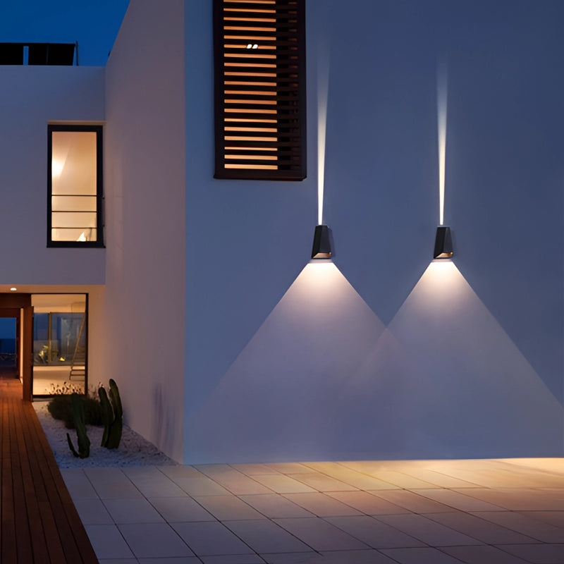 Pyramid-shaped LED wall sconce mounted on a wooden exterior near a window, providing a warm light that enhances the building's facade.