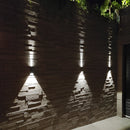 Modern waterproof outdoor pyramid LED wall sconce mounted on a wooden facade, featuring a rectangular and triangular design with shades and symmetrical elements, enhancing an urban street setting.