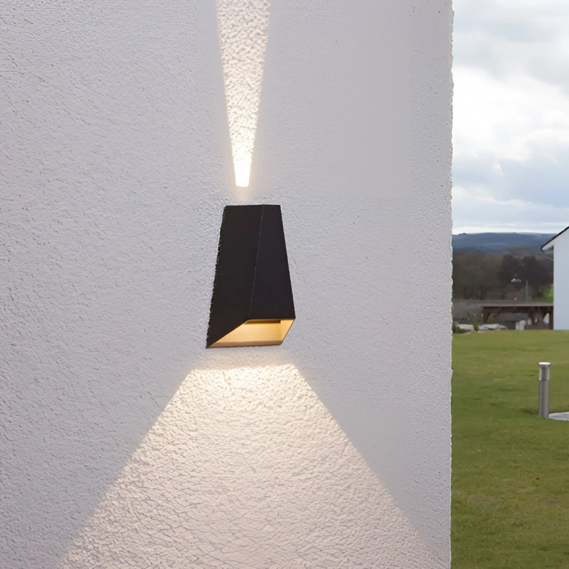 Outdoor pyramid-shaped LED wall sconce mounted on a concrete wall, surrounded by plants under a sky, featuring wood and composite materials.