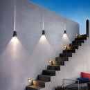 LED wall sconce mounted on a building exterior, featuring a pyramid design, emphasizing modern architectural elements like wood stairs and floors under varied lighting conditions.