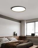 Minimalist circular LED ceiling light with a black rim, mounted on a ceiling in a modern, comfortable interior space with wooden elements and window blinds.