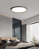 Circular LED ceiling light with black rim, minimalist design, mounted on ceiling in modern interior with wooden elements and bed frame.