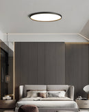 Circular LED ceiling light with black rim, minimalist design, energy-efficient, installed in a modern interior with white walls and wooden furniture.