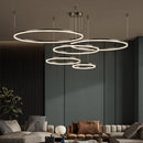 Circular LED pendant light with a gold finish and adjustable height chandelier hanging above a modern black couch, featuring multiple dimmable rings in various sizes.