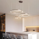 Circular LED pendant light with gold finish, featuring three adjustable rings in coffee color, suspended in a stylish interior setting.