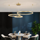 Circular LED pendant light with gold finish and adjustable height, featuring three dimmable rings (20cm, 40cm, 80cm) hanging above a modern table with plants and stylish interior design elements.