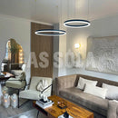 Gold finish circular LED pendant light chandelier with adjustable height, illuminating a modern living room with wooden flooring and comfortable furniture including a table and couch.